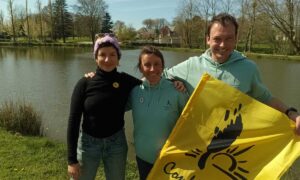 un homme et deux femmes au bord d'une rivière avec un drapeau de la Confédération Paysanne