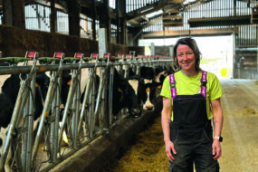 Une femme souriante près d'un cornadis autobloquant dans un bâtiment d'élevage abritant de vaches de race Prim'Holstein