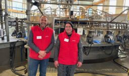 Deux éleveurs habllés d'une veste rouge devant leur manège de traite 28 postes de marque DeLaval