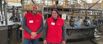 Deux éleveurs habllés d'une veste rouge devant leur manège de traite 28 postes de marque DeLaval