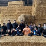Un homme et des enfants portant des bonnets noirs devant un mur de bottes de paille dans un élevage