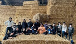 Un homme et des enfants portant des bonnets noirs devant un mur de bottes de paille dans un élevage