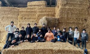 Un homme et des enfants portant des bonnets noirs devant un mur de bottes de paille dans un élevage