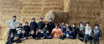 Un homme et des enfants portant des bonnets noirs devant un mur de bottes de paille dans un élevage