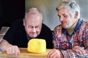 Deux hommes observent et sentent une motte de beurre artisanale posée sur une planche