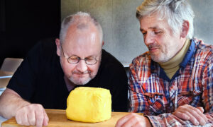 Deux hommes observent et sentent une motte de beurre artisanale posée sur une planche