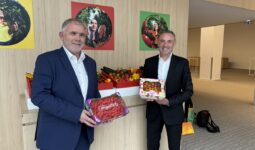 2 personnes dans un hall tenant des fraises et des tomates devant un étal de légumes