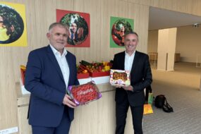 2 personnes dans un hall tenant des fraises et des tomates devant un étal de légumes