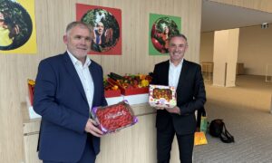 2 personnes dans un hall tenant des fraises et des tomates devant un étal de légumes