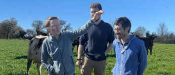 Une femme et deux hommes dans un champ avec des vaches. La femme est en train de parler en faisant des gestes