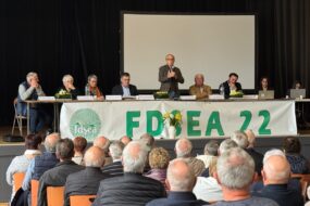 Huit personnes à la tribune d'une assemblée générale devant un public de séniors