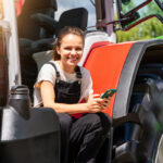 Une jeune femme souriante avec un portable à la main sur le marchepied d'un tracteur