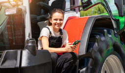 Une jeune femme souriante avec un portable à la main sur le marchepied d'un tracteur