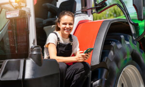 Une jeune femme souriante avec un portable à la main sur le marchepied d'un tracteur