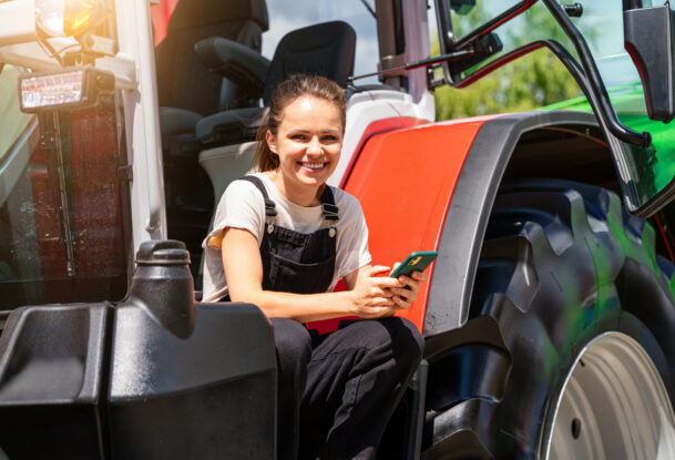 Une jeune femme souriante avec un portable à la main sur le marchepied d'un tracteur