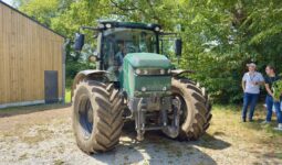 Un tracteur électrique dans une cour avec 2 hommes à l'ombre d'un arbre qui le regarde