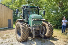 Un tracteur électrique dans une cour avec 2 hommes à l'ombre d'un arbre qui le regarde