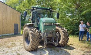 Un tracteur électrique dans une cour avec 2 hommes à l'ombre d'un arbre qui le regarde