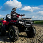 Une personne équipée (casque, gants, veste..) sur un quad dans un champ