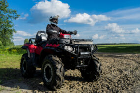 Une personne équipée (casque, gants, veste..) sur un quad dans un champ