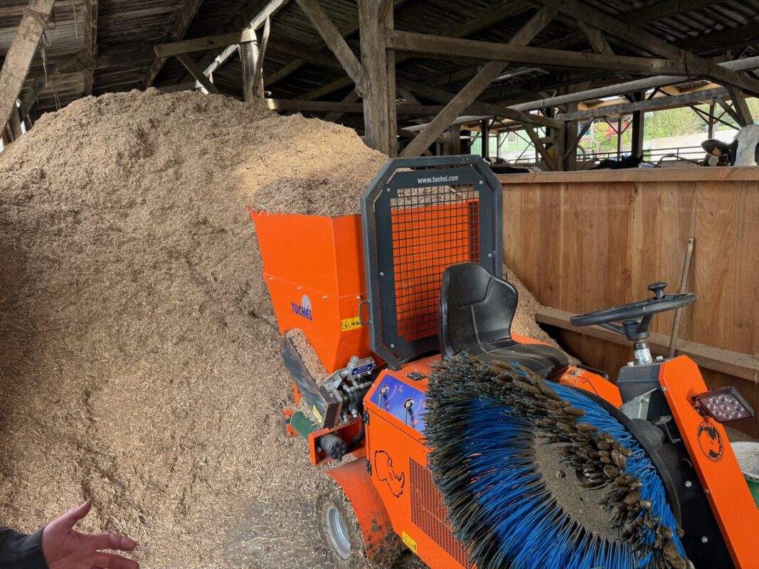 Un matériel automoteur d'entretien de logettes devant un tas de miscanthus dans un élevage bovin