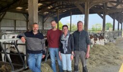 Trois hommes et une femme posenty devant la table d'alimentation d'un bâtiment d'élevage abritant des génisses de race Montbéliarde