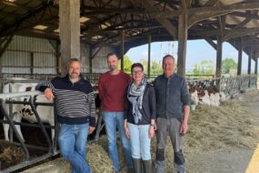 Trois hommes et une femme posenty devant la table d'alimentation d'un bâtiment d'élevage abritant des génisses de race Montbéliarde