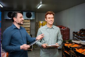 Deux hommes souriants discutent dans une chambre froide remplie de légumes