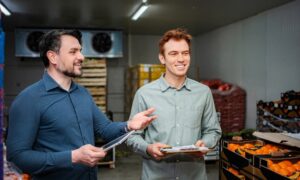 Deux hommes souriants discutent dans une chambre froide remplie de légumes