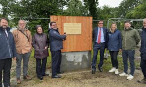 Un groupe de personne devant la première planche posée d'un bâtiment en construction