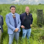 Un groupe de personne dans les herbes hautes devant un arbre tout juste plantée