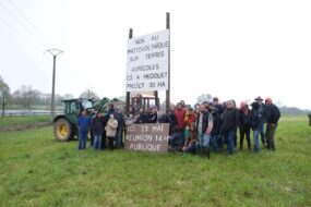 Un groupe de manifestant autour d'un panneau planté dans un champ