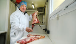 Un boucher en blouse et charlotte dans un atelier de préparation de la viande