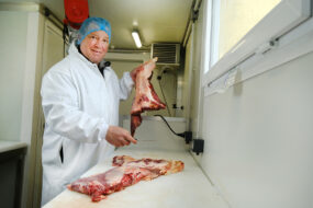 Un boucher en blouse et charlotte dans un atelier de préparation de la viande
