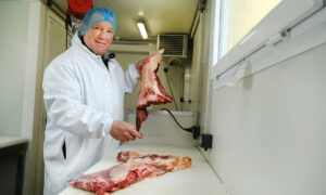 Un boucher en blouse et charlotte dans un atelier de préparation de la viande