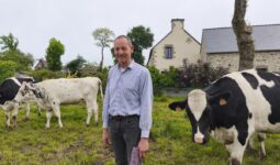 Un homme souriant au milieu des vaches dans un champ attenant à une maison