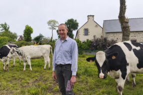 Un homme souriant au milieu des vaches dans un champ attenant à une maison
