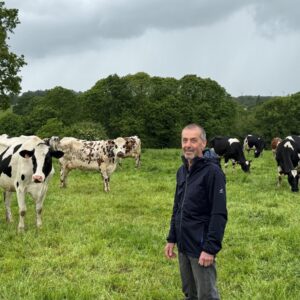 Un éleveur souriant au milieu d'un troupeau de vaches laitières au pâturage
