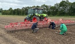 Trois hommes vérifient l'état du sol pour ajuster le réglage d'une roto-étrille tirée par un tracteur