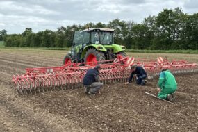 Trois hommes vérifient l'état du sol pour ajuster le réglage d'une roto-étrille tirée par un tracteur
