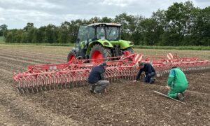 Trois hommes vérifient l'état du sol pour ajuster le réglage d'une roto-étrille tirée par un tracteur