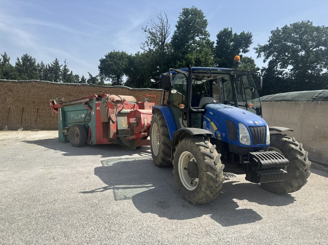 Une désileuse pailleuse attelée à un tracteur garé devant le front d'attaque d'un silo de maïs ensilage