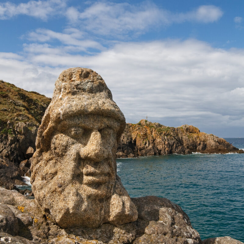 Un visage avec un bonnet sculpté sur rocher en bord de mer
