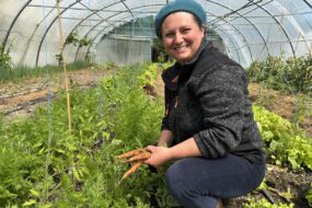 Une femme souriante accroupie dans une serre avec des carottes avec des carottes dans les mains