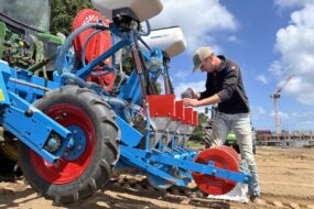 Une personne remplit un semoir atteé à un tracteur dans un champ