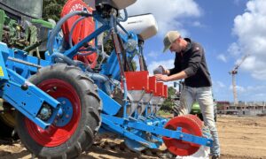 Une personne remplit un semoir atteé à un tracteur dans un champ