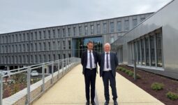 Deux hommes en costume sombre et cravate devant un bâtiment gris