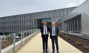 Deux hommes en costume sombre et cravate devant un bâtiment gris