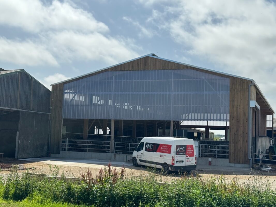 Une camionnette garée devant un bâtiment bardé de matière translucide dans un élevage laitier