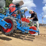 Un homme entrain de remplir un semoir attelé à un tracteur dans un champ